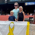 A woman and two children holding a yellow ribbon banner outdoors.