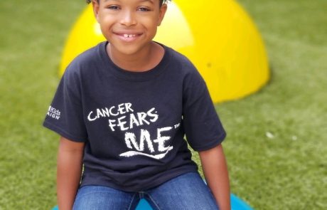 Smiling child sitting on a blue ball outdoors.