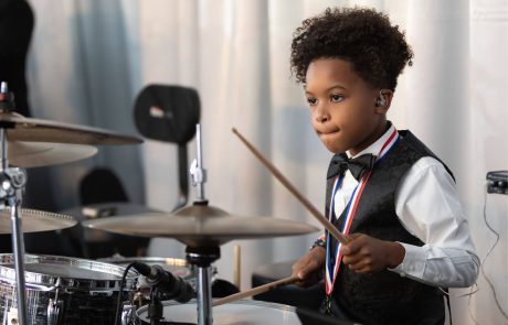 Young boy in formal wear playing drums with focus.
