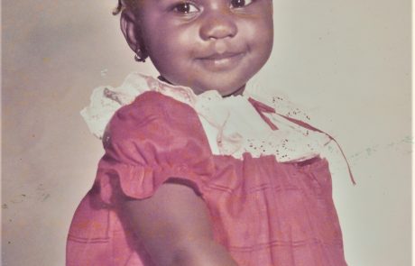 A young girl in a red dress smiling at the camera.