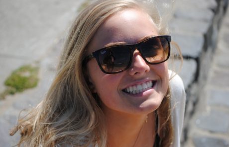 Smiling woman wearing large sunglasses in natural light.
