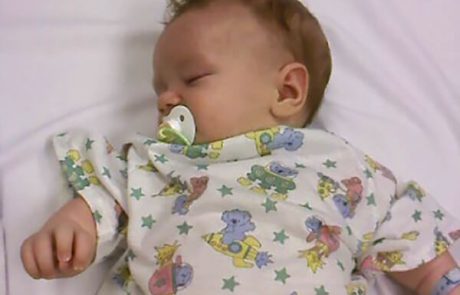 Sleeping baby with a pacifier in a colorful onesie.