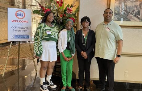 Four people posing together indoors with floral decorations in the background.