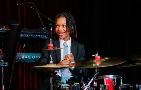 A young drummer in a suit smiling behind a drum set.