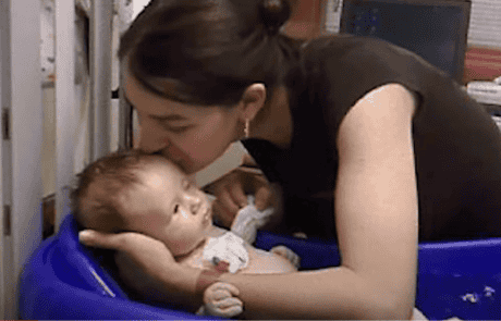 A woman lovingly kisses a baby lying on a cushion.