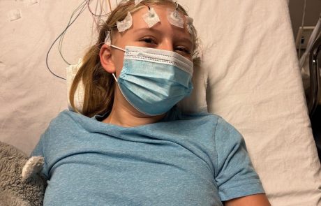 Young girl lying in a hospital bed wearing a mask and head electrodes.