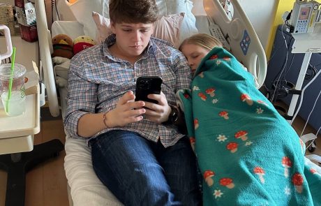 Young man sitting casually with a phone, next to a covered figure in a colorful blanket.