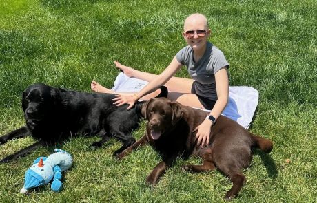 A girl relaxing on grass with two dogs on a sunny day.