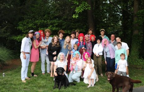 A large group of people posing outdoors with two dogs on a sunny day.