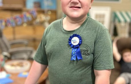 Smiling boy wearing a blue ribbon and holding a display.