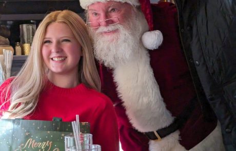A girl smiling with Santa Claus and another person indoors.
