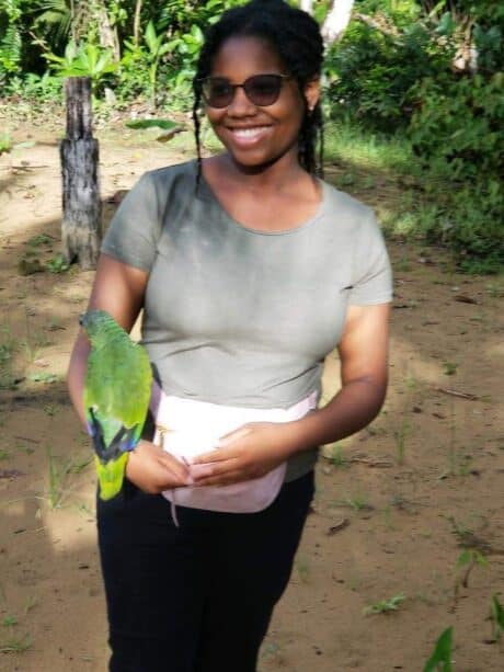 A smiling woman holding a green parrot outdoors.