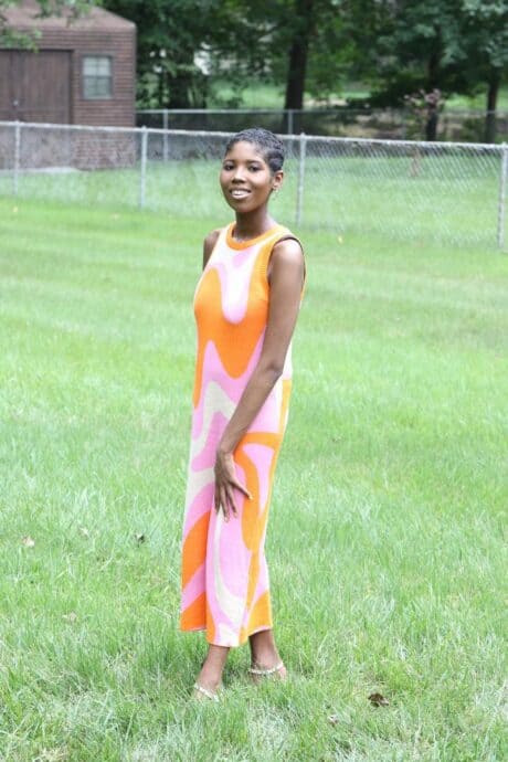 Woman in a colorful dress standing on green grass outdoors.