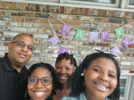 A joyful family selfie with a birthday banner in the background.