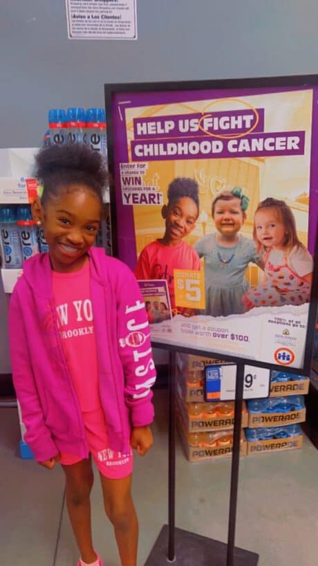 Young girl posing by a childhood cancer awareness poster.