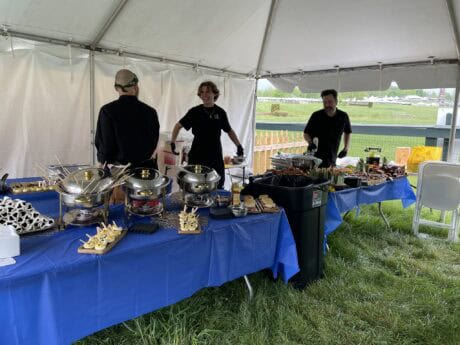 Three people stand behind a table of baked goods at an outdoor event tent.