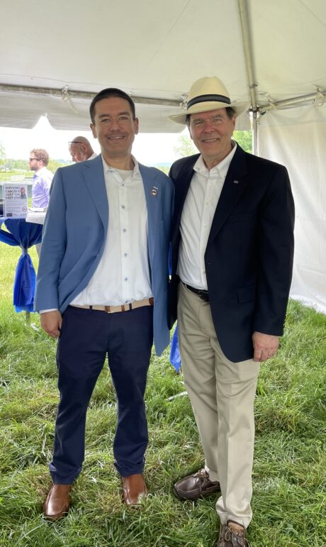 Two men in blazers standing outdoors, smiling for a photo.