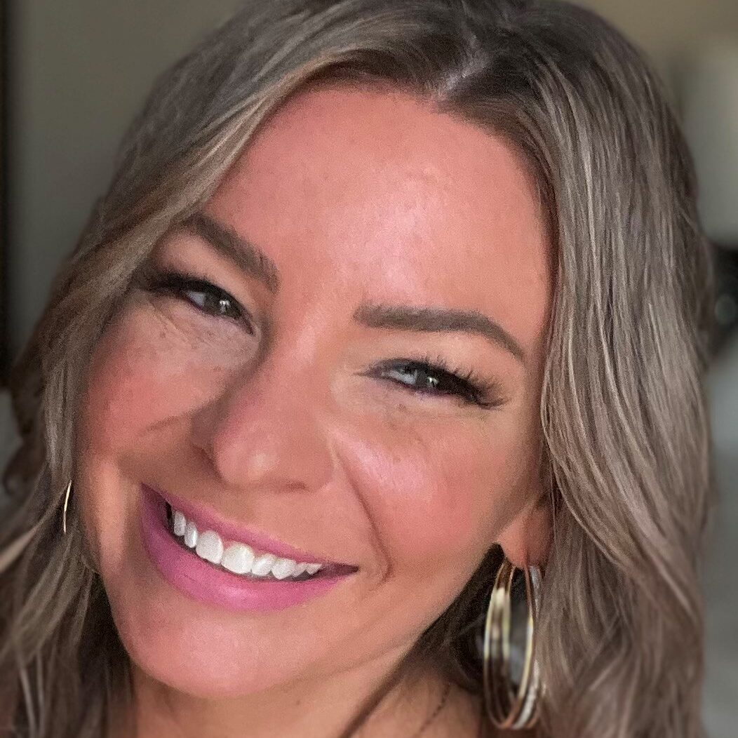 Smiling woman with light brown hair and gold earrings.