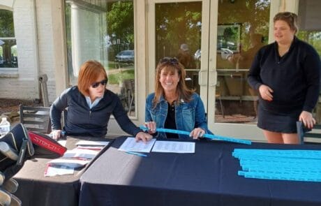 Three women working at an event registration table outside a building.