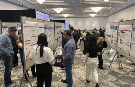 People discuss research at an indoor academic poster session.