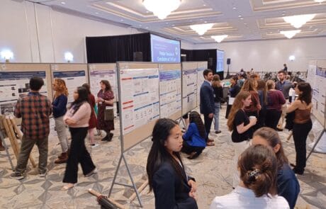 A busy conference room with people networking and viewing a large board.