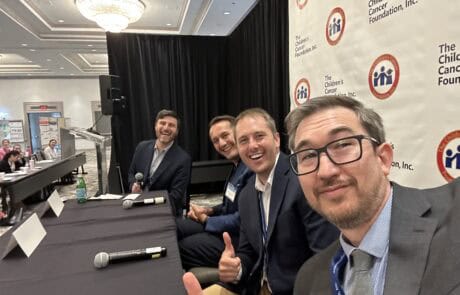 Four men in suits posing happily at a conference table with microphones.
